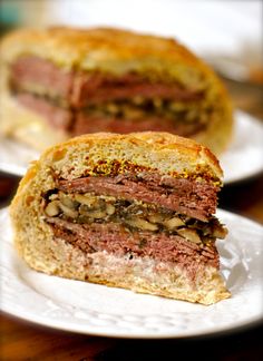 a meat sandwich cut in half on a plate with another sandwich behind it and the rest of the sandwich visible