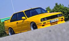 a yellow car parked on the side of a road next to some bushes and trees