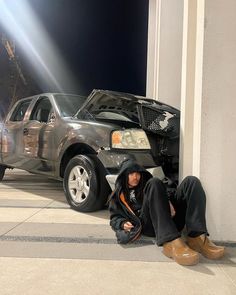 a man sitting on the ground next to a car with it's hood up