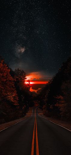 an empty road at night with the sun setting in the distance and stars above it