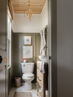 a white toilet sitting in a bathroom next to a sink and wooden cabinet under a chandelier