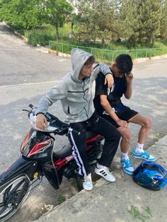 two young men sitting on a motorcycle talking on the phone while another man sits next to them