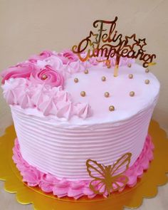 there is a pink cake with gold lettering on it and flowers in the bottom tier