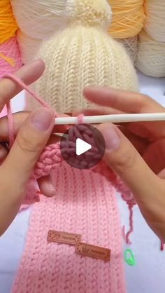 two hands holding yarn and knitting needles with balls of yarn in the background