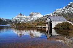 a small house sitting in the middle of a lake surrounded by snow covered mountains and trees