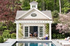 a small pool house with an outdoor lounge area next to it and a swimming pool surrounded by trees