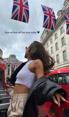 a woman standing in front of a red car with british flags flying above her head