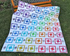 a colorful quilt sitting on top of a green grass covered field next to a wooden bench