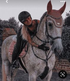 a woman riding on the back of a brown and white horse next to a brick wall