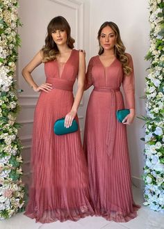 two women in long dresses standing next to each other with flowers on the wall behind them