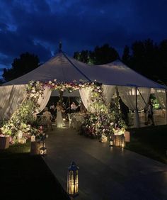 a wedding tent with flowers and lanterns lit up at night