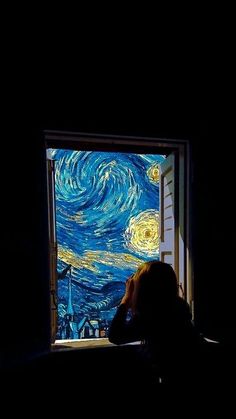 a person sitting in front of a window looking at the starry night painting on it