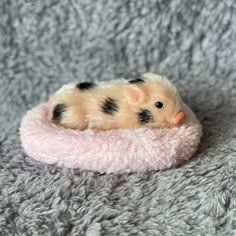 a small toy hamster laying on top of a pink blanket covered in grey and white fur