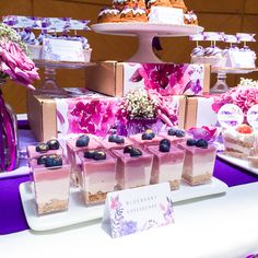 there are many desserts on the table with purple and pink flowers in vases