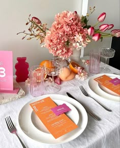 the table is set with pink and orange flowers, silverware, and menu cards