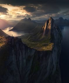 an aerial view of the mountains and water at sunset, with a person standing on top