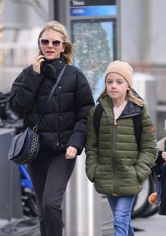 a mother and daughter walking down the street while talking on their cell phones, both wearing winter coats