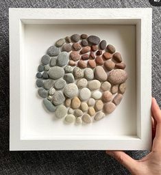 a hand holding a white frame with rocks arranged in the shape of a heart on it