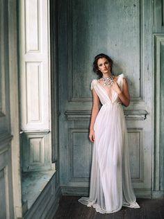 a woman in a white dress standing next to a wall with a necklace on her neck