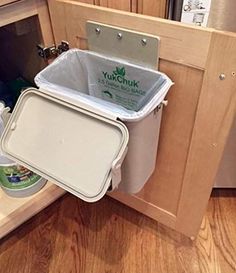 the kitchen cabinet door is open to reveal an ice chest and trash can in it