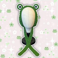 a crocheted green frog hat on top of a white mannequin's head