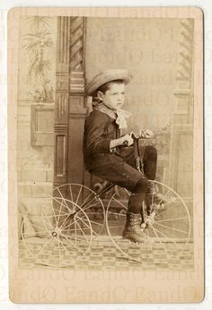 an old photo of a young boy sitting on a tricycle with his hat on