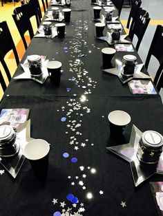 a long table is decorated with silver stars and confetti on black cloths