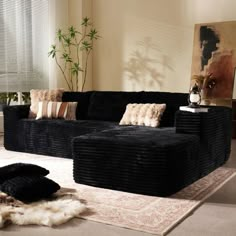 a living room filled with black couches and pillows on top of a white rug