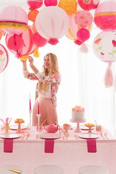 a woman standing in front of a table filled with pink and yellow paper lantern decorations