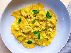 a white plate topped with ravioli and corn covered in pesto sauce, garnished with green leaves