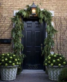 two large planters filled with green apples sit in front of a door decorated for christmas