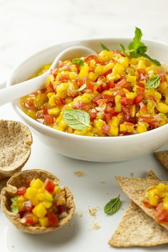 a white bowl filled with corn and salsa next to tortilla chips