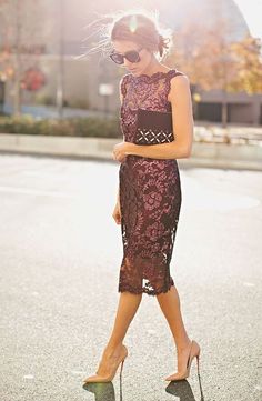 a woman walking down the street wearing high heels and a lace dress with an open back