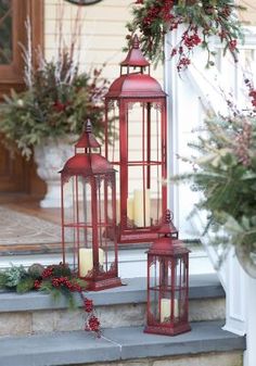 two red lanterns sitting on top of a step next to christmas wreaths and greenery