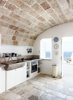 a kitchen with an arched ceiling and stone flooring, along with white cabinets and counter tops