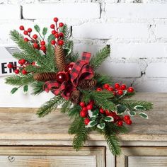 a christmas wreath with pine cones and red berries on it sitting on top of an old dresser