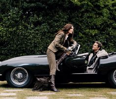 a woman sitting on top of a car next to a man