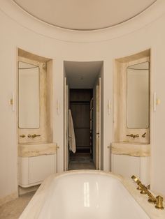 a large bath tub sitting next to two sinks in a bathroom under a round mirror