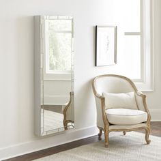 a white chair sitting in front of a mirror on the wall next to a window