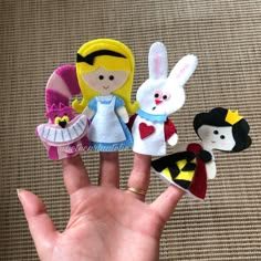 the hand is holding four small dolls in different colors and sizes, including one with a princess on it