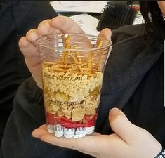 a person holding up a cup filled with cereal and other things to eat in it