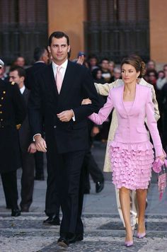 a woman in a pink dress walking next to a man in a black suit