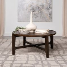 a coffee table with a vase and books on it in front of a large painting