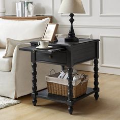 a black end table with a basket underneath it and a lamp next to it on a wooden floor