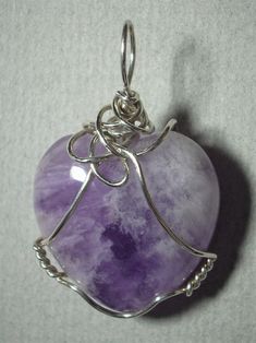 Amethyst Heart Pendant Wire Wrapped in .925 Sterling Silver Round Wire An ennobling stone heart of varied white, clear and light transparent purple coloration with multiple internal reflecting and refracting crystal planes; it especially compliments pink, purple, red, burgundy, and blue colors of clothing, wears well with light to dark color combinations, appearing darker purple against darker backgrounds; The heart shape may appeal to a purist view, but a visible crystal plane pattern, and vari Lavender Stone Jewelry Gift, Spiritual Heart Cut Jewelry For Healing, Sterling Silver Crystals With Natural Stones As Gift, Clear Jewelry With Large Stone As A Gift, Handmade Silver Jewelry With Heart Cut, Silver Healing Crystals, Silver Gemstone Crystals For Jewelry Making, Clear Large Stone Jewelry For Gifts, Silver Amethyst Crystals For Jewelry Making