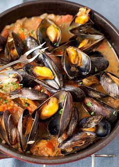 a pan filled with mussels and sauce on top of a table