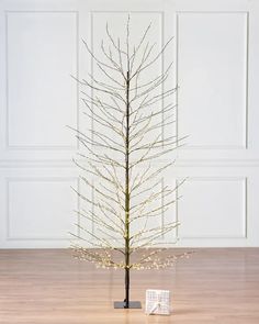 a small christmas tree with white lights on it's branches in front of a wall