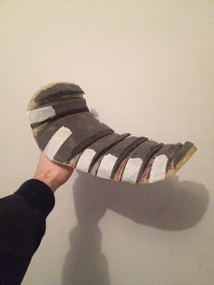 someone is holding up a shoe that has been made out of strips of wood and paper