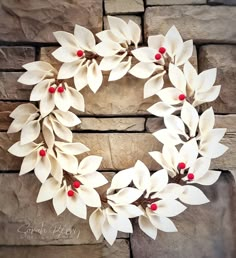 a wreath with white flowers and red berries hanging on a stone wall in front of a brick wall