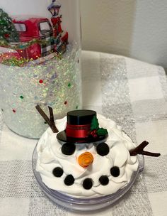 there is a frosted snowman on the table next to a glass jar with christmas decorations